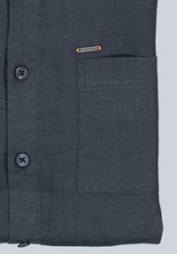 Himmelblaues Leinenhemd mit einer Brusttasche, Knopfverschluss und einem orangefarbigen Metallanhänger. Glatte Textur und schlichtes Design.