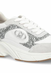 Basket blanc avec un accent pailleté argenté et des détails en daim gris. Dispose d'une fermeture à lacets, d'une tige texturée et d'un logo argenté. Semelle épaisse.