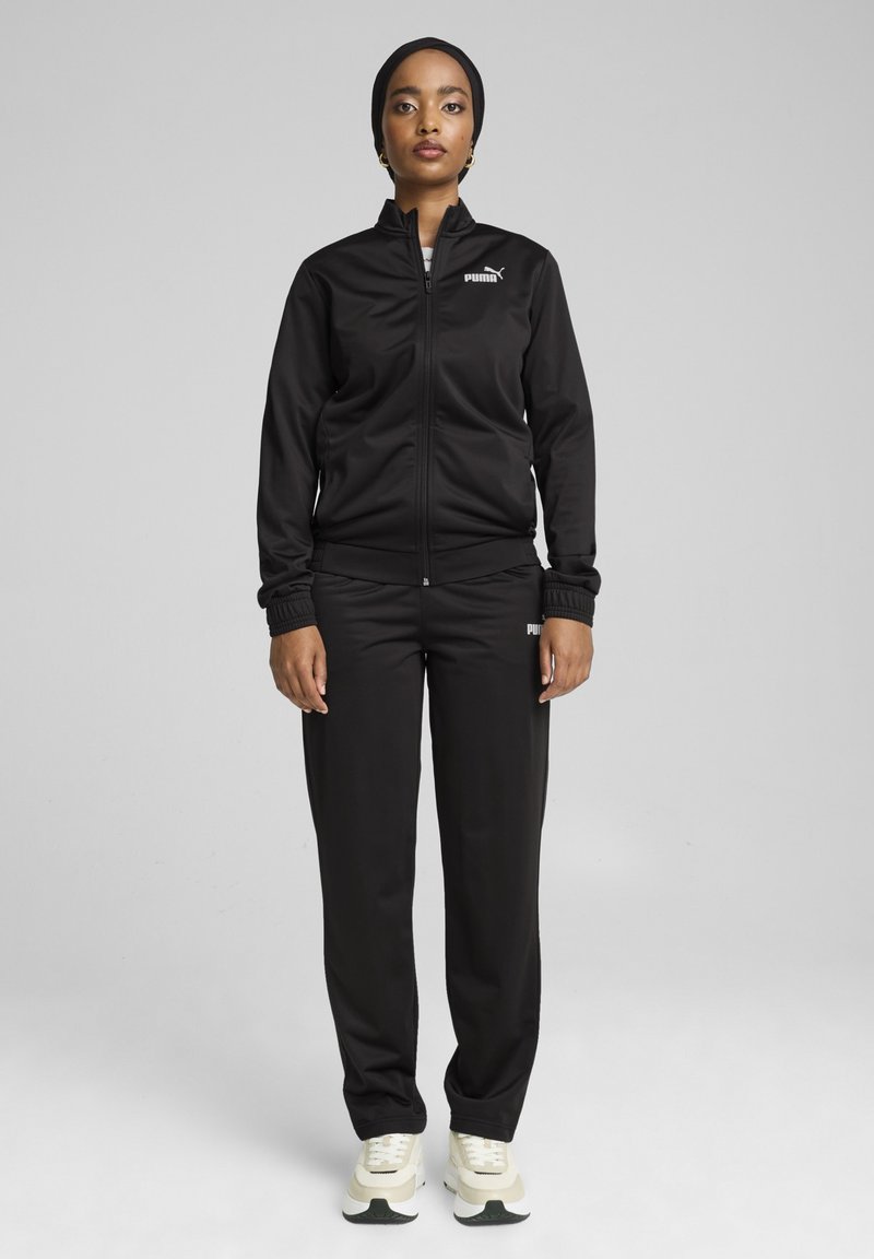 Melnas sporta uzvalks no gludas auduma ar rāvējslēdzēja jaku un elastīgām aprocēm, ar mazu balto Puma logotipu. Saskaņots ar baltām un zaļām sporta kurpēm.