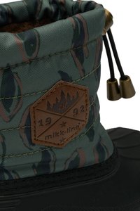Bota impermeable con un patrón en verde y marrón que presenta un upper texturizado, suela de goma y un parche de cuero marrón con un diseño de montaña.