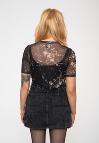 Sheer black top with short sleeves, featuring a splatter pattern in light brown; paired with a dark denim mini skirt with pockets.