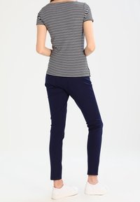 Haut à manches courtes rayé en bleu marine et blanc, associé à un pantalon ajusté bleu marine et des baskets blanches. Tissu lisse et coupe décontractée.