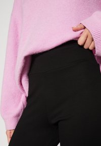 Light pink, fluffy sweater with ribbed cuffs, paired with black, fitted leggings. Focus on texture and color contrast.