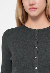 Tmavě šedý žebrovaný kardigan s kulatým výstřihem a sedmi kovovými knoflíky vpředu, předvádějící měkkou, textura látku.