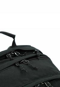 Černý látkový batoh s několika zipovými kapsami a elegantními šňůrkami s kovovými prvky. Texturovaný povrch s minimalistickými designovými detaily.