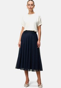 Jupe en tulle marine avec un design en couches, associée à un chemisier crème à manches bouffantes. Des talons beige complètent le look.