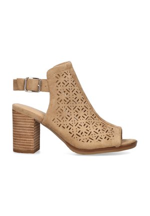 Sandalias de tacón bloque en ante beige con recortes geométricos, punta abierta, correa al tobillo con hebilla de metal y un tacón de madera texturizada.