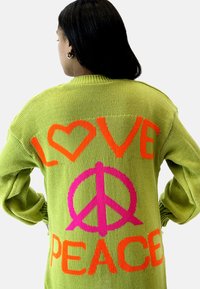 Stickad tröja i ljusgrönt med stor, kontrasterande text: "LOVE" i orange och "PEACE" i rosa, med ett hjärta och en fredssymbol.