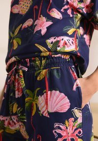 Ensemble de pyjama marine à motifs floraux comprenant de grands flamants roses, des plantes tropicales et des coquillages. Taille élastique avec détail de lien ajustable. Tissu doux.
