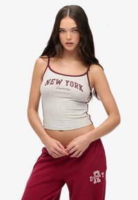 Graues, kurzes Tanktop mit kastanienbraunem Besatz, versehen mit dem Druck "NEW YORK" in fetter, lässiger Schrift. Kombiniert mit kastanienbraunen Hosen mit weißen Akzenten.
