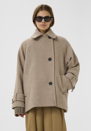Cappotto di lana beige con chiusura a bottoni, colletto ampio e grandi tasche. Presenta maniche oversized con polsini regolabili e una vestibilità rilassata.