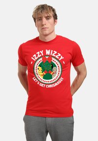 Červené tričko s krátkým rukávem, které obsahuje kulatý grafický motiv s vánočním designem, včetně zeleného stromu a textu "IZZY WIZZY - PŘEJME SI VÁNOCE."