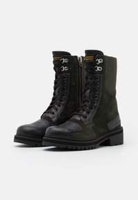 Botas de combate de gamuza verde oscuro con punta de cuero negro, cuello acolchado y ojales de metal. Cierre lateral para ponerlas fácilmente. Suela gruesa.