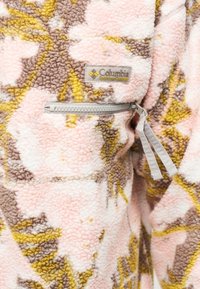 Ήπιο φλις ύφασμα με ροζ, κίτρινο και καφέ λουλουδάτο σχέδιο, με τσέπη με φερμουάρ σε γκρι χρώμα και μπαλώματα λογότυπου Columbia Sportswear Company.