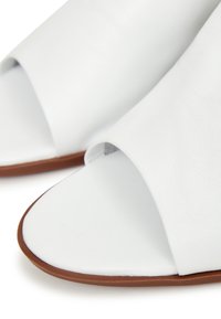 Valkoiset nahkasaappaat, joissa on avoin varvasdesign, sileä pinta ja ruskea pohja. Ylähengessä on minimalistinen tyyli ilman koristeita.