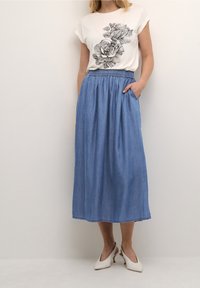 Bílé tričko s černým květinovým potiskem; doplněné modrou džínovou maxi sukní s elastickým pasem a bočními kapsami.