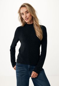 Černý sweater s dlouhým rukávem a vysokým výstřihem, vyrobený z měkké pleteniny. V kombinaci s modrými džíny, které mají jemnou texturu a detaily.