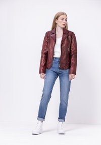 Rote Leder-Bikerjacke mit silbernen Reißverschlüssen, kombiniert mit hellblauen Jeans und weißen High-Top-Sneakern. Darunter ein einfaches, weißes T-Shirt mit Rundhalsausschnitt.