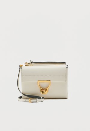 Petit sac bandoulière en cuir crème avec une lanière réglable et une boucle en forme de D dorée sur le rabat avant.