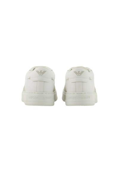 Zapatillas blancas con un acabado suave, presentando un logo sutil en el talón y costuras en tono. Diseño de corte bajo con puntera redondeada.