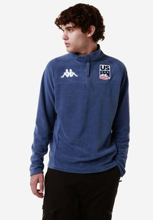Pullover in fleece blu navy con zip a quarti e logo Kappa e emblema degli Stati Uniti. Presenta una consistenza morbida e maniche lunghe, progettato per il comfort.