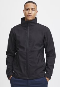 Zwarte softshell jas met een hoge kraag, voorkant met rits en twee zijzakken. Gladde textuur met een getailleerde pasvorm en geen zichtbare patronen.