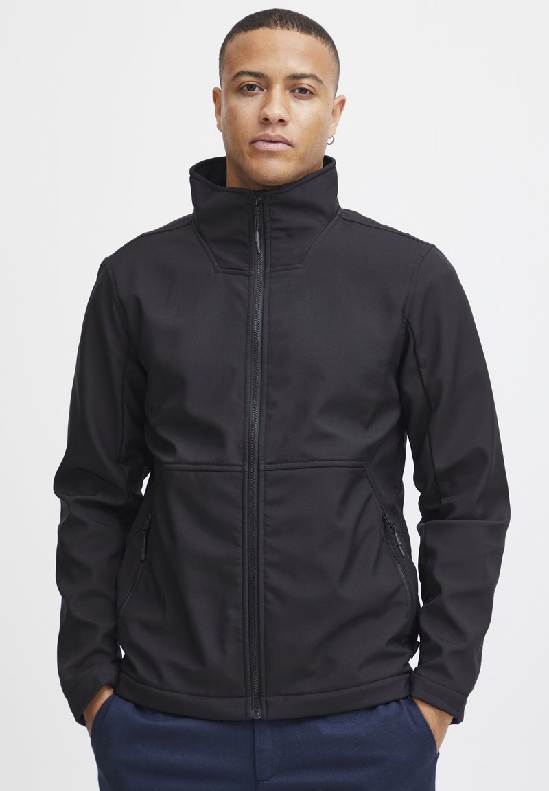 Zwarte softshell jas met een hoge kraag, voorkant met rits en twee zijzakken. Gladde textuur met een getailleerde pasvorm en geen zichtbare patronen.