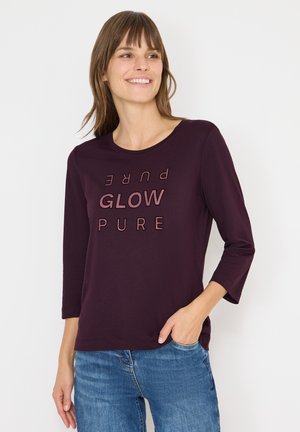 Bordowa koszula z długim rękawem, okrągłym dekoltem i nadrukowanym tekstem "GLOW PURE" w różnych wielkich literach. Miękka tkanina, luźny krój, casualowy styl.