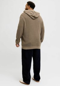 Beige pletená mikina s texturovaným vzorem, širokou kapucí a ribbovanými manžetami, v kombinaci s námořnickými kordovými kalhotami a bílými teniskami.