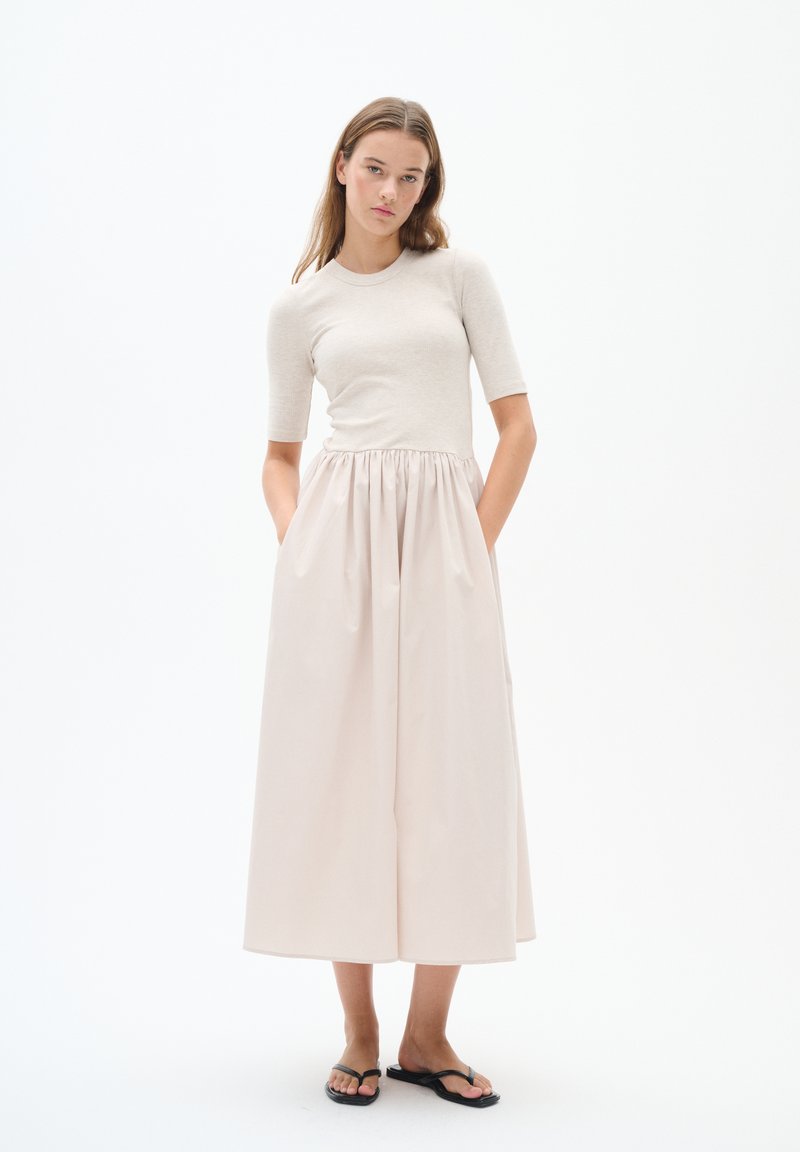 Helle beigen Ripp-Top mit kurzen Ärmeln, kombiniert mit einem fließenden, blassen rosa Maxikleid mit elastischem Bund und Seitentaschen.