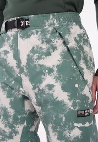 Groene en witte spetterpatroon skibroek met verstelbare tailleband en zwart beslag. Bevat een logopatch op de linker dij.