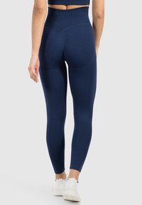 Navy hoge taille legging met een gladde, stretchachtige textuur, voorzien van een V-vormige naad aan de achterkant en een strakke pasvorm tot aan de enkel.