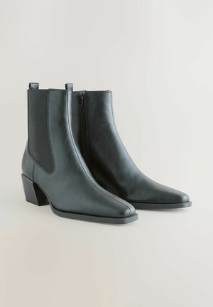 Stivali alla caviglia in pelle nera con punta appuntita, zip laterale e tacco largo. Presentano pannelli elastici sui lati per una facile calzata.