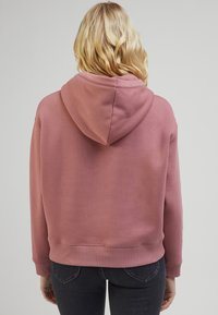 Sweat à capuche ample rose avec capuche à cordon, poignets et ourlet côtelés, en matière douce mélangée en coton, présenté de dos.