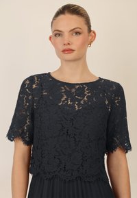 Navyblauw kanttop met bloemenpatroon, korte mouwen en geribbelde zoom. Gekoeld met een geplooide rok, gladde stofstructuur.