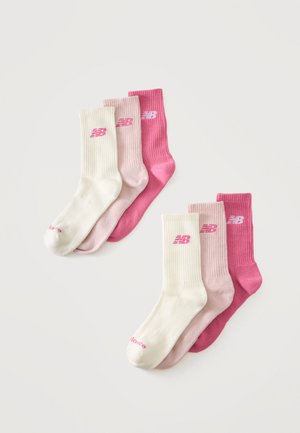 Six paires de chaussettes New Balance en blanc, rose clair et rose foncé, disposées en deux groupes qui se chevauchent sur un fond blanc.