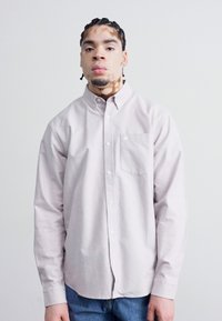 Chemise boutonnée rose clair à manches longues, avec une poche avant et une texture lisse, associée à un jean en denim bleu.
