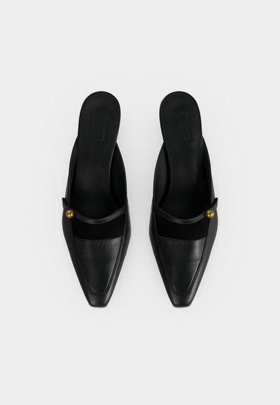 Ζευγάρι μαύρα δερμάτινα παπούτσια τύπου slip-on με μυτερά δάχτυλα, με λεπτό λουράκι στο πάνω μέρος που ασφαλίζεται με ένα χρυσό κουμπί σε κάθε πλευρά.