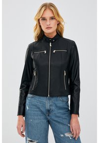 Black leather cropped jacket with a high collar, front zip, and two zippered chest pockets. Features gold hardware and stitching details.