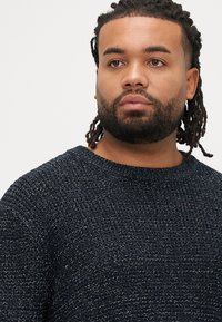 Tamsiai mėlynas megztinis su tekstūruotu paviršiumi. Suteikia apvalią kaklo iškirptę ir ilgus rankovėlius. Audinyje subtiliai įterpti metaliniai akcentai.