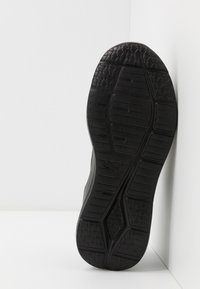 Zwarte sportieve schoenzool met textuurrubber, hexagonale patronen, gripgroeven en een logodetail.
