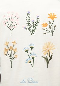 Έξι κεντημένα μπουμπούκια αγριολούλουδων σε παστέλ αποχρώσεις τοποθετημένα σε δύο σειρές πάνω σε λευκό ύφασμα, με το κέντημα "Les Deux" από κάτω.