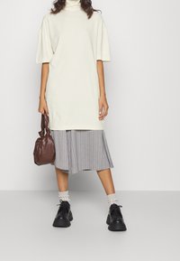 Cremefarvet oversized kjole med korte ærmer og høj krave, lagd oven på en grå pinstripe nederdel. Sorte sko og en brun håndtaske fuldender looket.