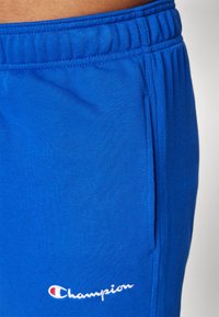 Blå bomull idrettsshorts med elastisk midjebånd, sidelommer og en liten hvit "Champion"-logo brodert på benet.