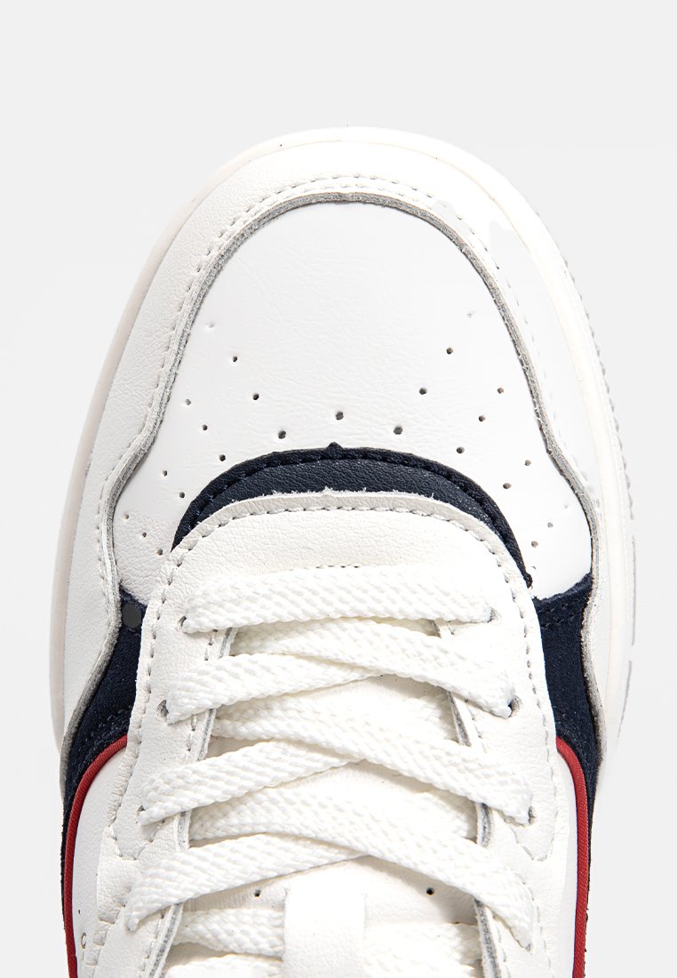 Witte sneaker met marineblauwe en rode accenten, gladleren bovenkant, ronde neus, geperforeerde details en platte veters.