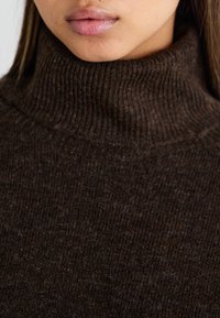 Maglione a collo alto marrone a coste con una texture morbida e un colletto aderente, caratterizzato da una leggera lucentezza e dettagli di design minimi.