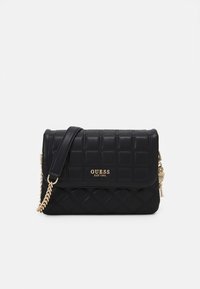 Černá prošívaná kožená taška Guess přes rameno se zlatým řetízkem, klopovým uzávěrem a zlatou destičkou s logem s nápisem "GUESS EST 1981".