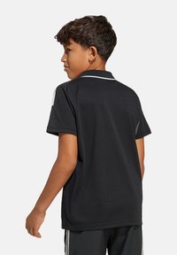Polo nero con dettagli bianchi, maniche corte e colletto. Il tessuto appare liscio con un design aderente. Marchio visibile sulla spalla.