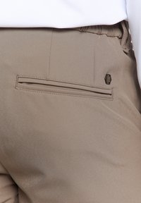 Lichtbruine broek met een gladde textuur, voorzien van een achterzak met verborgen stitching en een klein logoaccent.