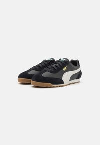 Svart- och grå sneakers med mocka- och lädermaterial, en yttersula i gummirik och vita accenter med en logotyp på sidan.